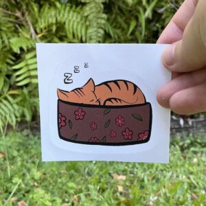 Orange cat sleeping in brown bascet bed wit h flowers on it.